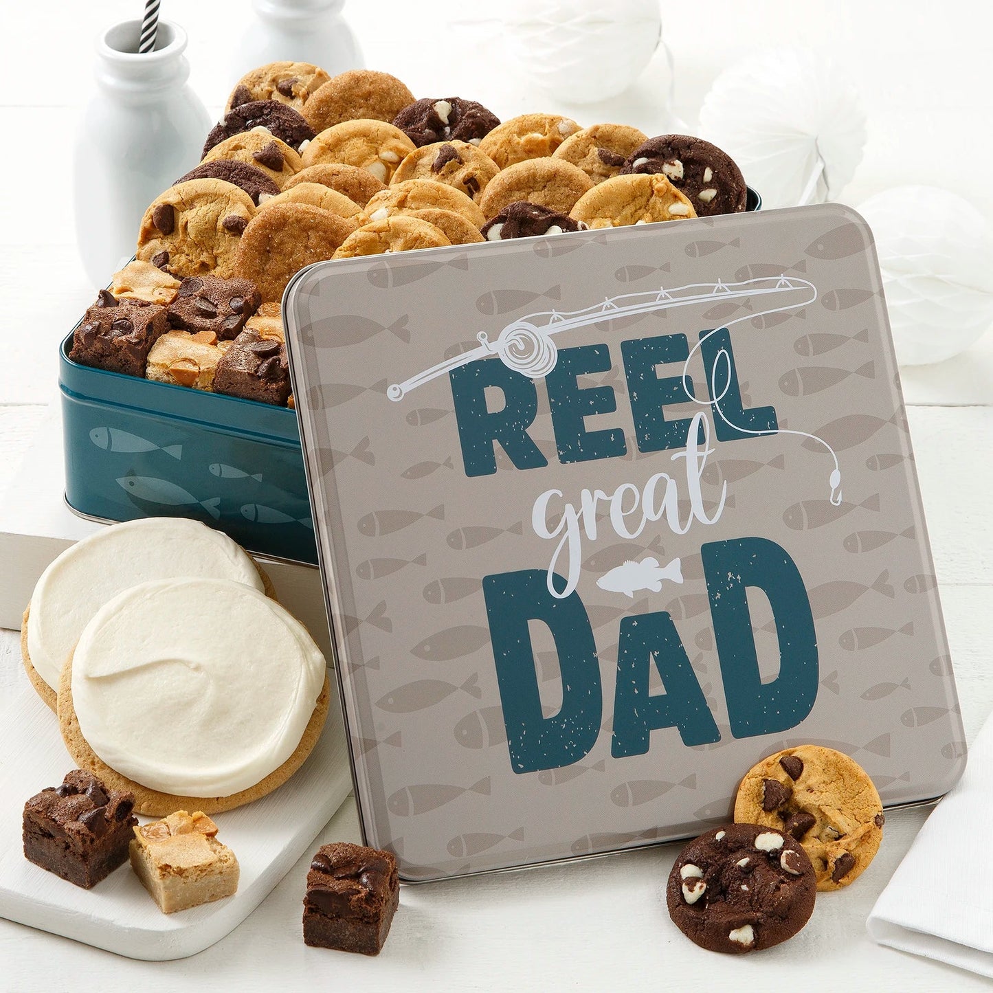 Reel great Dad Father's Day tin featuring an image of a fishing rod and fish. Inside the tin is an assortment of nibblers bite-sized cookies, brownie bites and two frosted natural round cookies. 